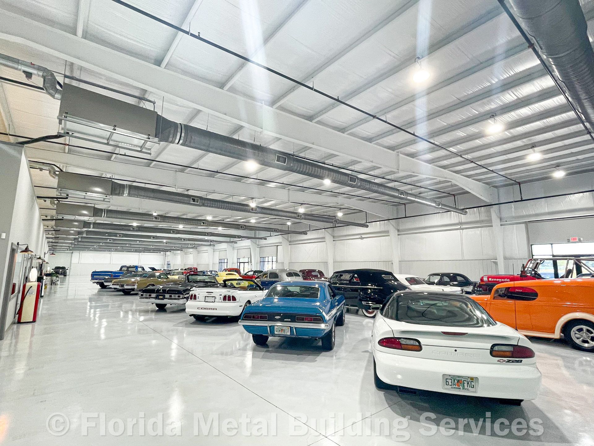 A large indoor car storage facility with a white ceiling and polished floor, housing numerous classic and modern cars.