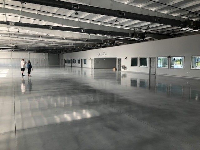 Two people walk across a large, open industrial space with a highly polished gray concrete floor and white walls.