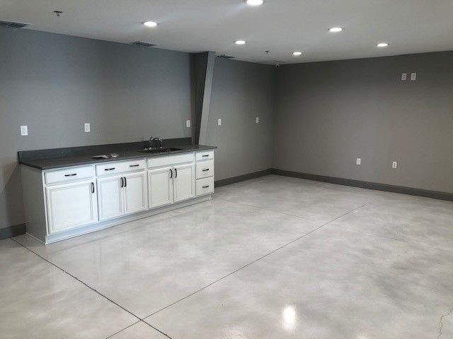 A modern room with grey walls and polished concrete floors featuring a white kitchenette with a dark grey countertop.