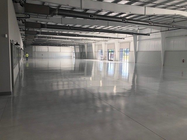 A wide, empty warehouse with polished grey concrete floors, high ceilings with exposed ductwork, and white walls.