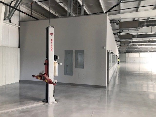 An Atlas automotive lift stands against a grey wall in a large, modern industrial warehouse with a polished concrete floor.