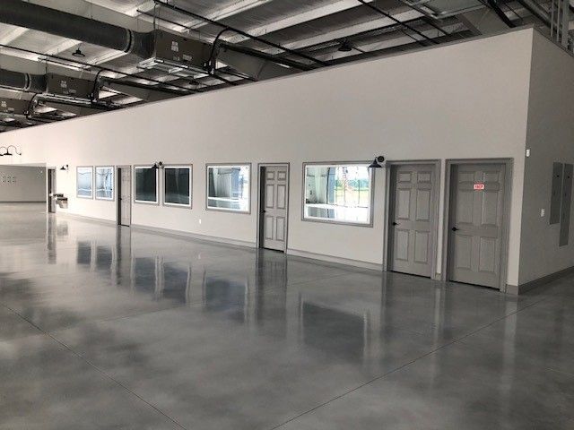 A spacious, modern warehouse interior with polished gray concrete floors, white walls, multiple windows, and two gray doors.