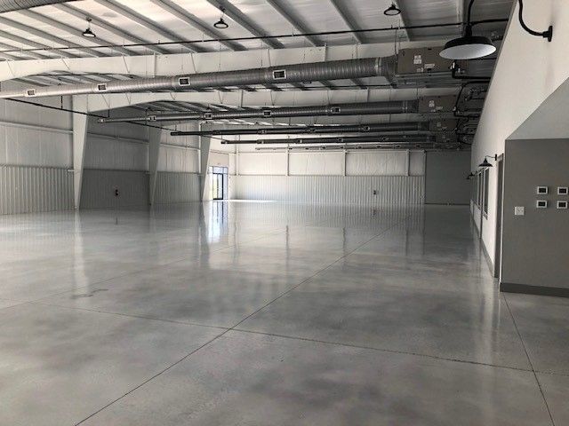 A wide-angle, interior view of a large, empty industrial warehouse with polished concrete floors and high ceilings.