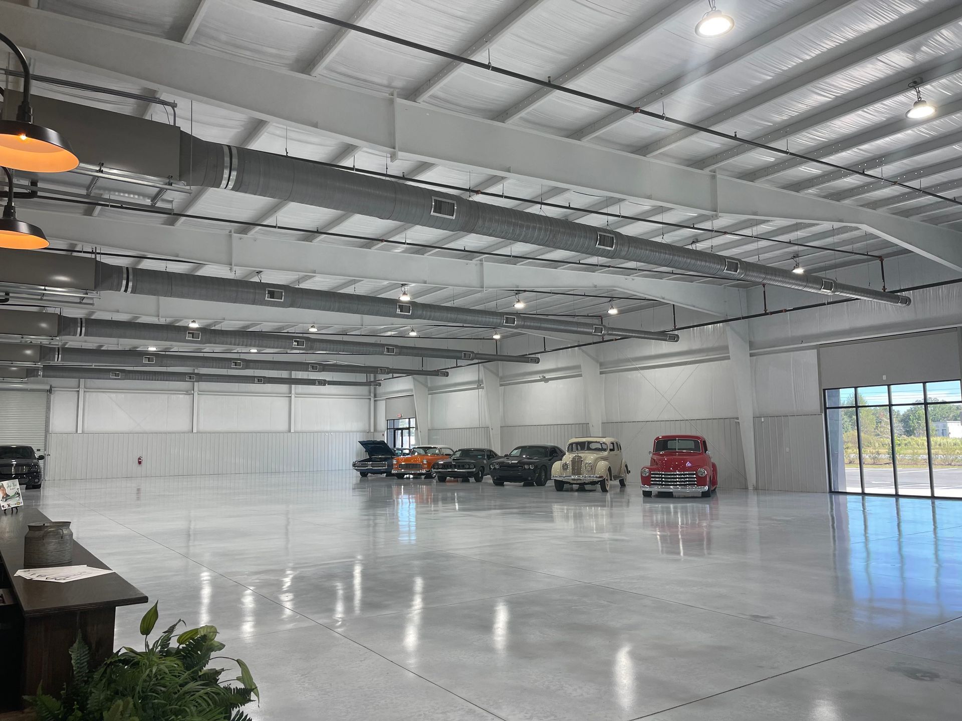 A large, well-lit warehouse with a polished concrete floor displaying several classic cars parked against a back wall.