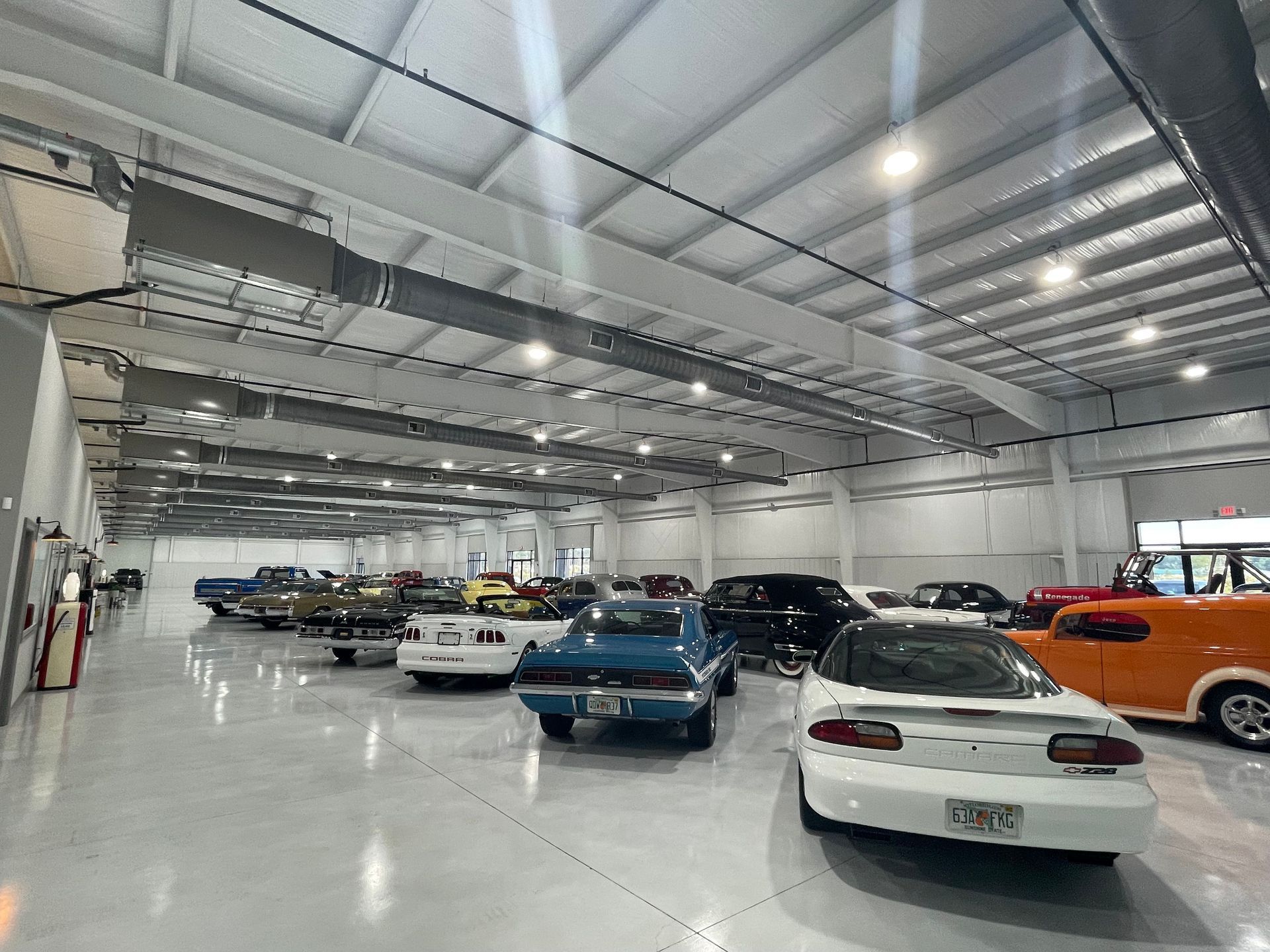 A bright, spacious indoor garage containing a collection of classic and modern cars parked on a polished concrete floor.