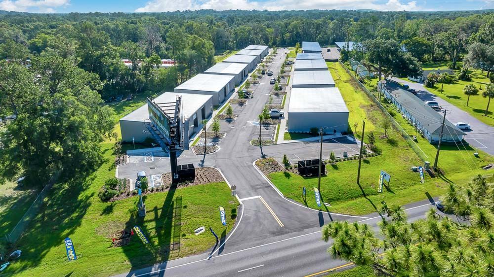 Aerial view of a suburban park with white pavilions, roads, and lush green trees.