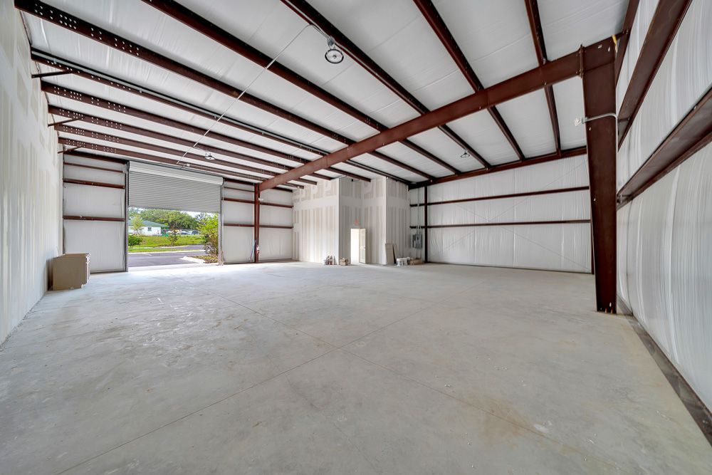 Empty steel-framed warehouse interior with concrete floor and open bay door to outside