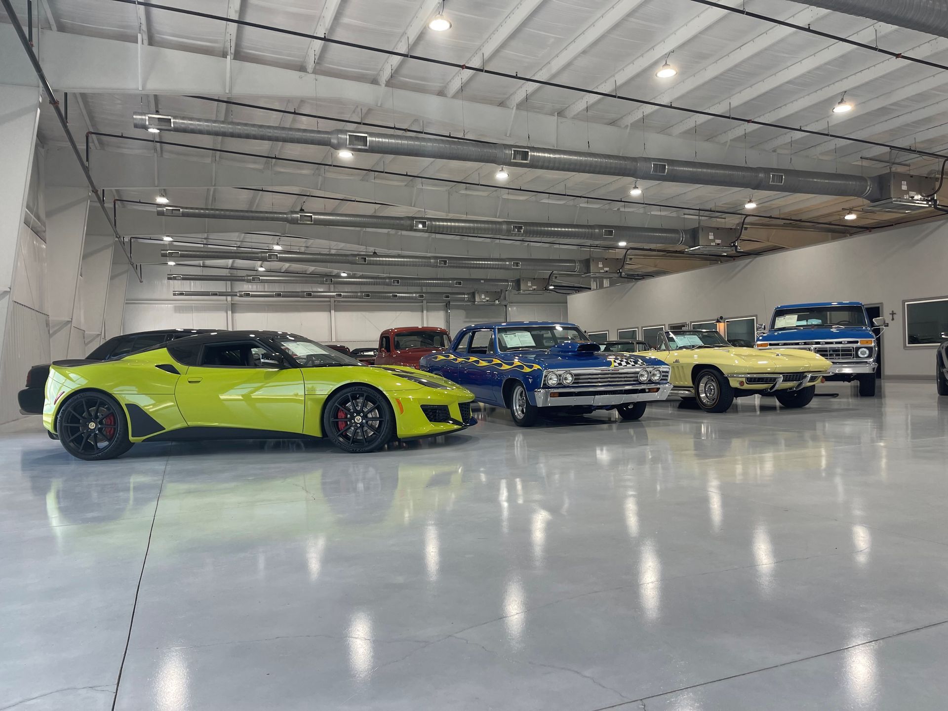 Bright lime green sports car with classic blue and cream cars parked in a spacious showroom
