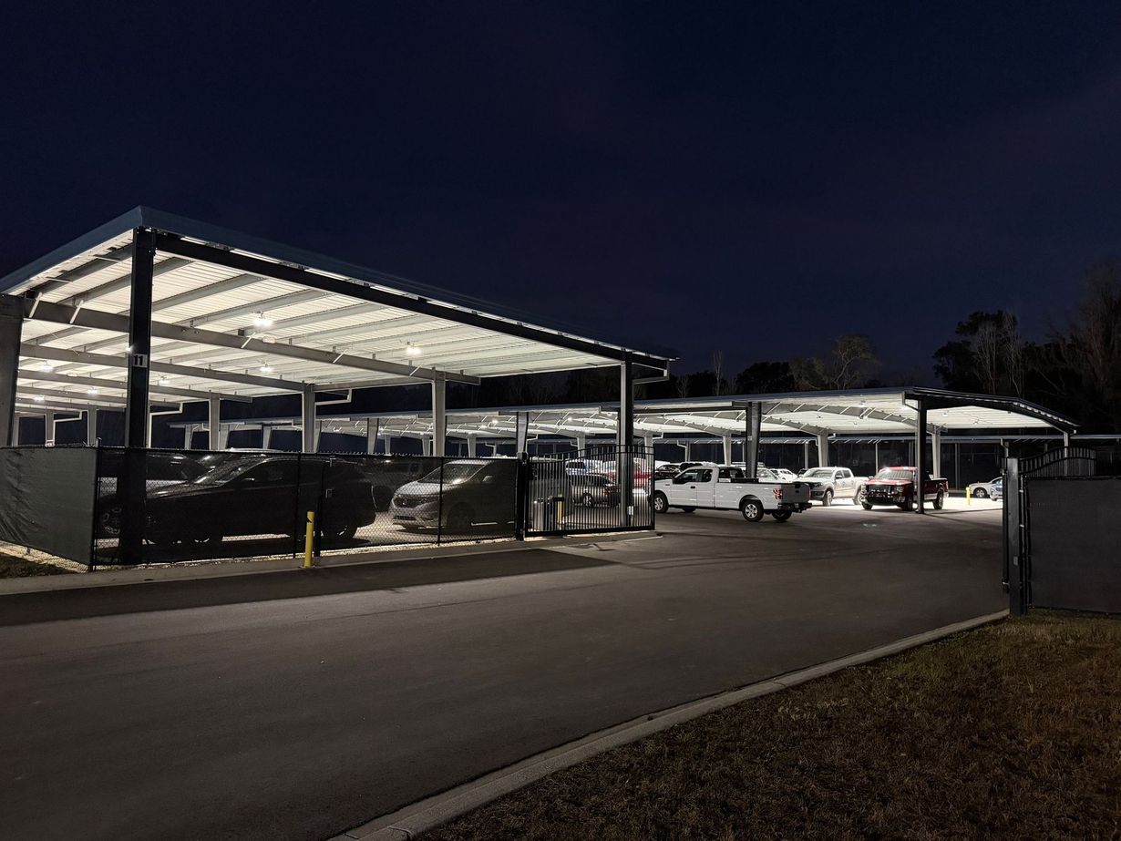 A parking lot at night featuring illuminated solar panel carports sheltering several parked vehicles.