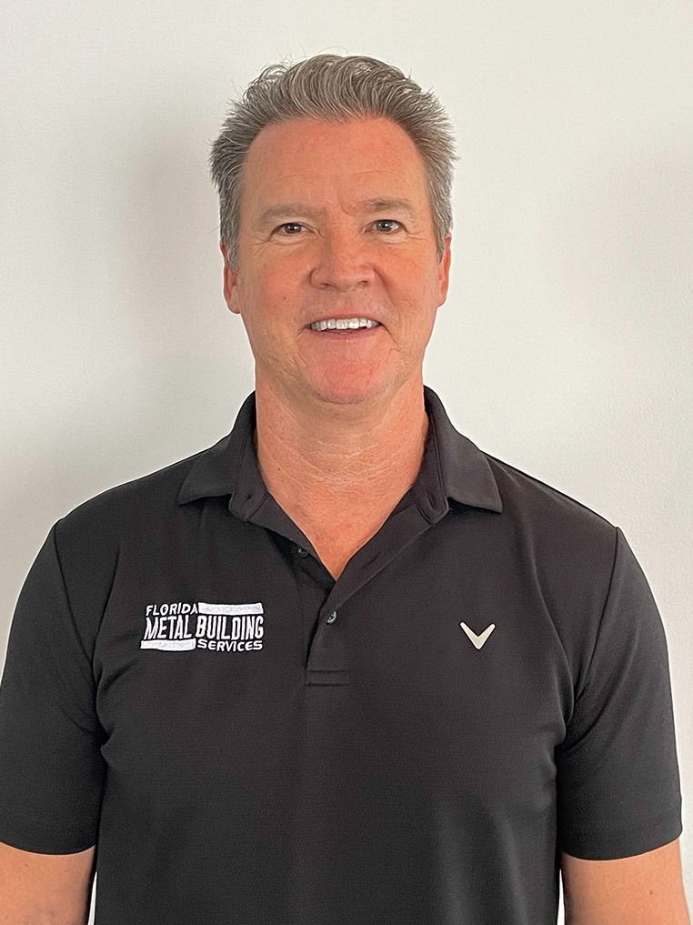 A person with short, light brown hair smiling, wearing a black collared polo shirt with a white logo on the chest.
