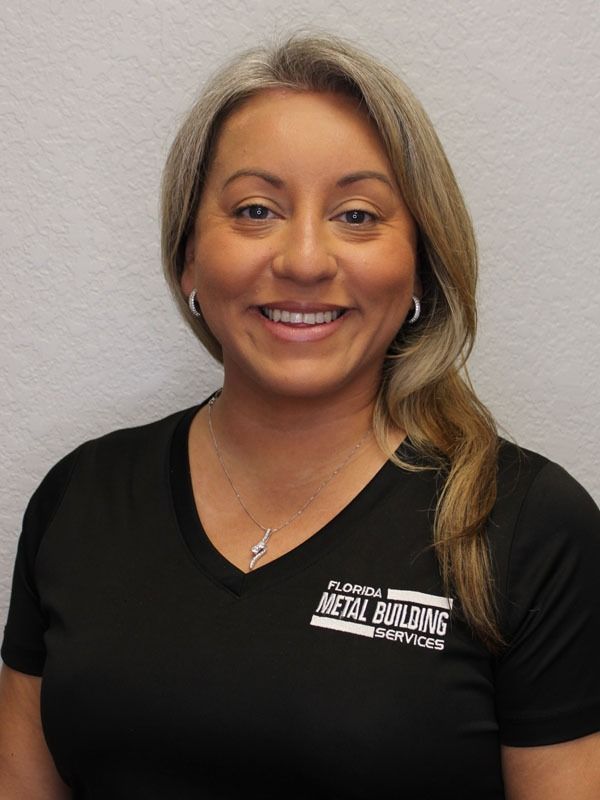 A smiling person wearing a black v-neck shirt with a white logo, posed against a plain, light-colored background.
