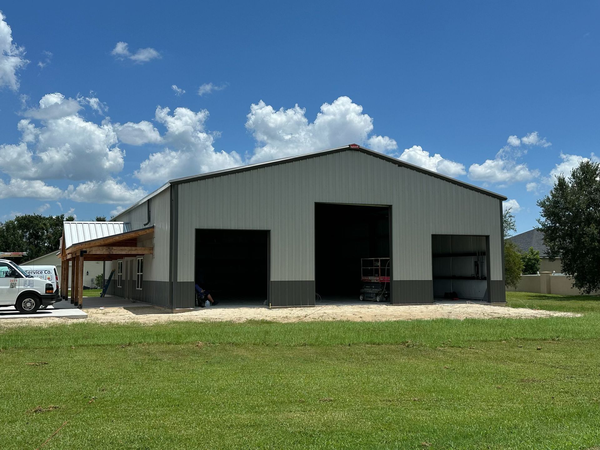 Large gray metal warehouse with open bays and a small side awning, under a blue sky with clouds.