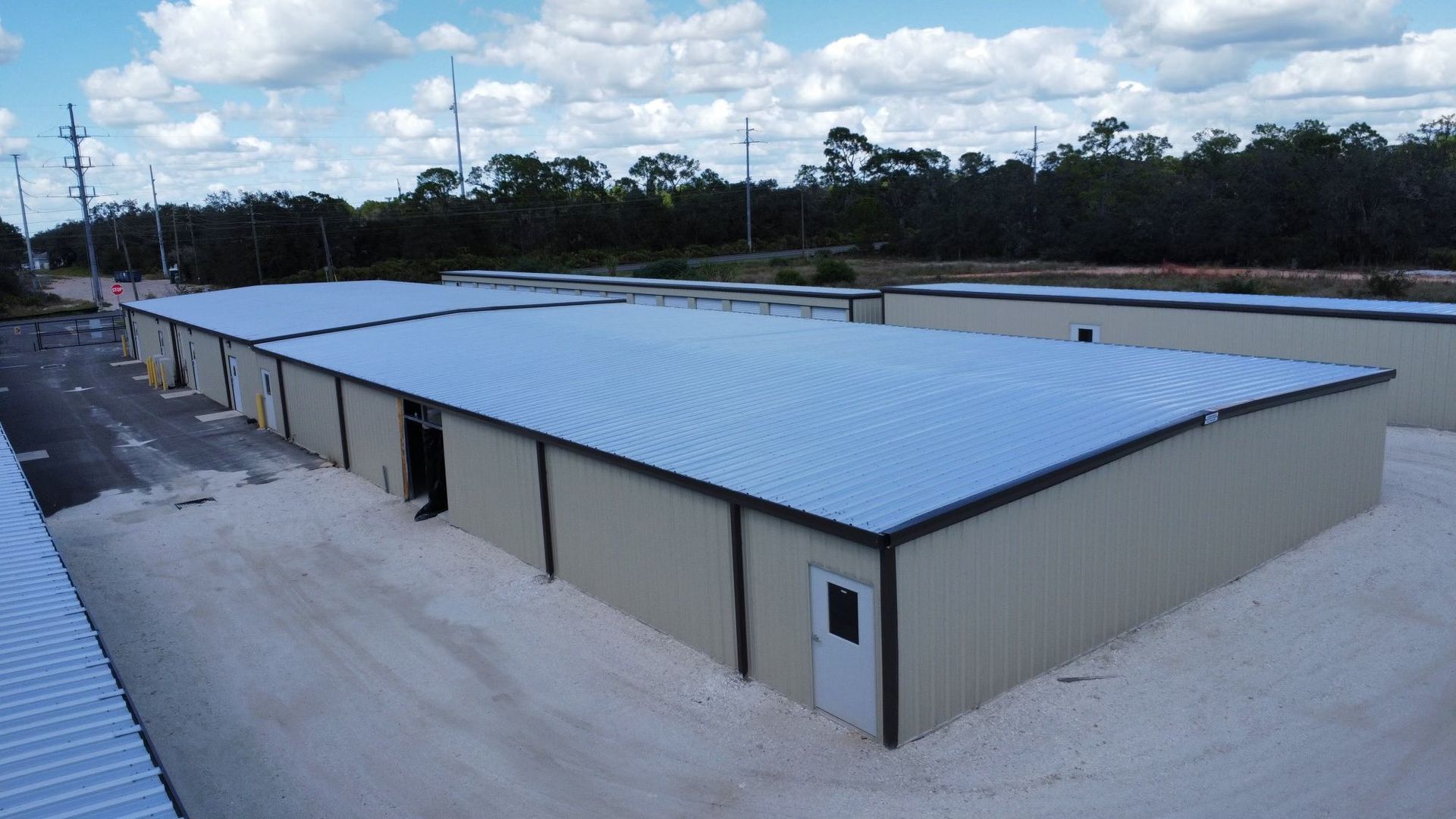 Large beige warehouse with a blue metal roof on a concrete lot, viewed from the corner.