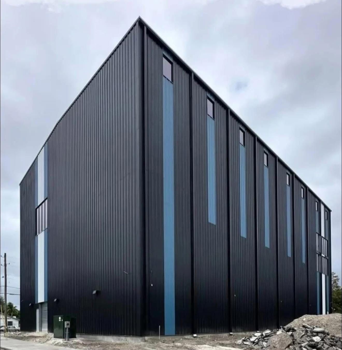 Black corrugated metal industrial building with tall narrow windows under an overcast sky.