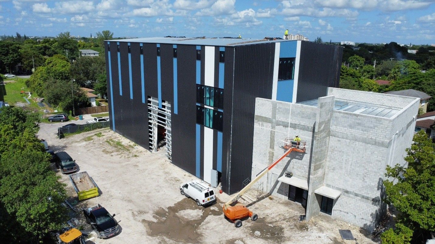 Aerial view of a black-and-white building under construction with a crane and parked vehicles nearby.
