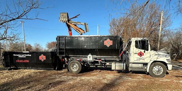 A black dumpster truck with a raised arm, used for debris removal, on a sunny day.