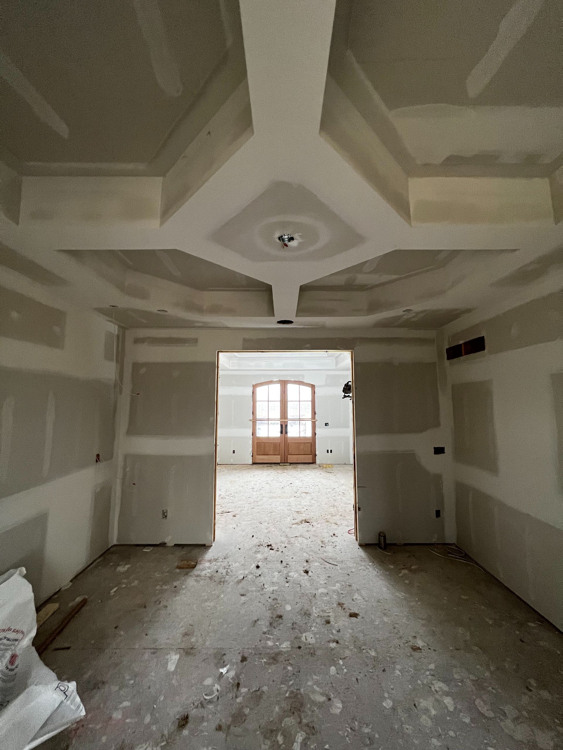 Interior room under construction with ornate ceiling design, drywall walls, and wooden double doors.