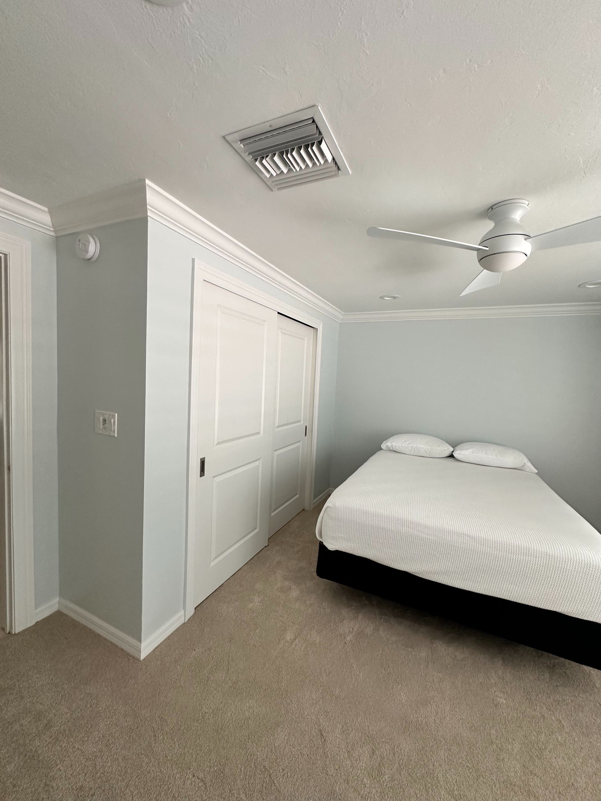 Bedroom with a bed, white closet doors, light blue walls, and a ceiling fan.