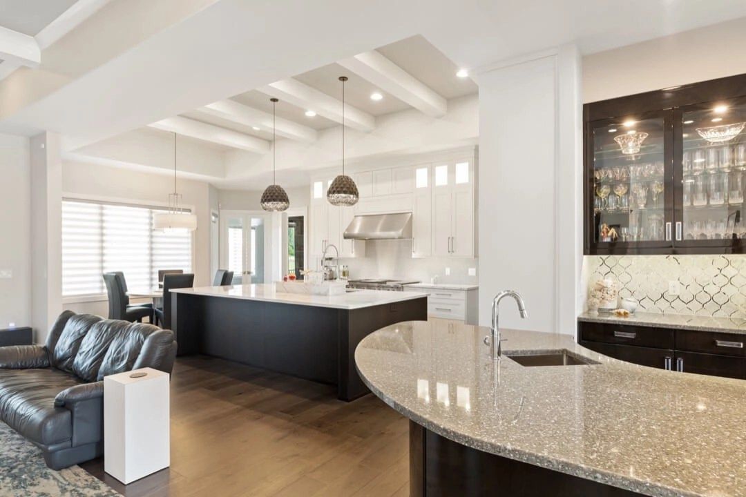 Open-concept kitchen with dark island, light countertops, and a built-in bar with glass cabinets.