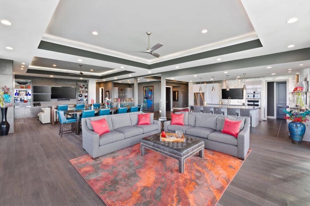 Open-concept living area with gray sofas, orange rug, dining table, kitchen, and a decorative ceiling.