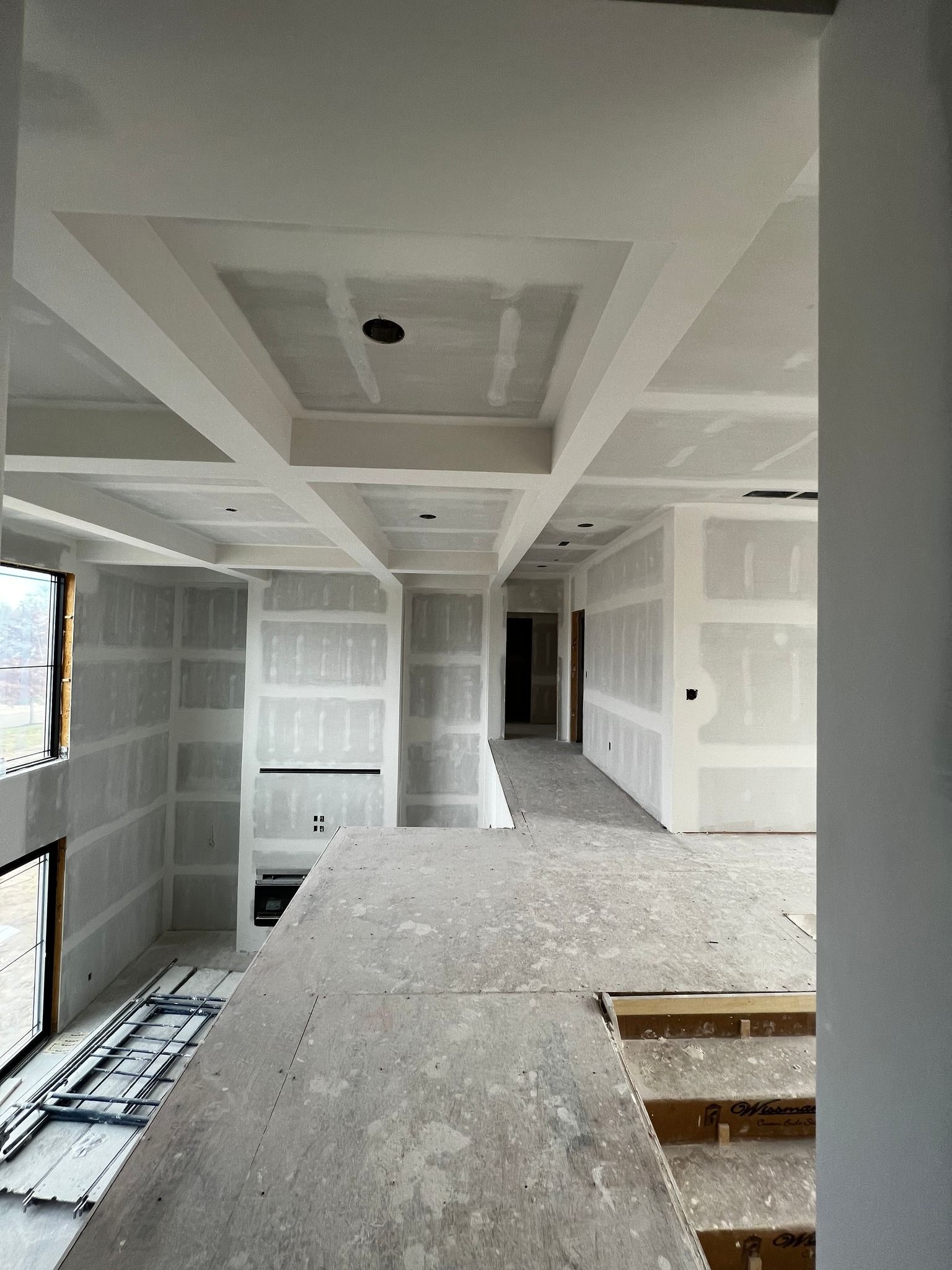 Interior of a building under construction, showing drywall, ceiling beams, and a concrete floor.