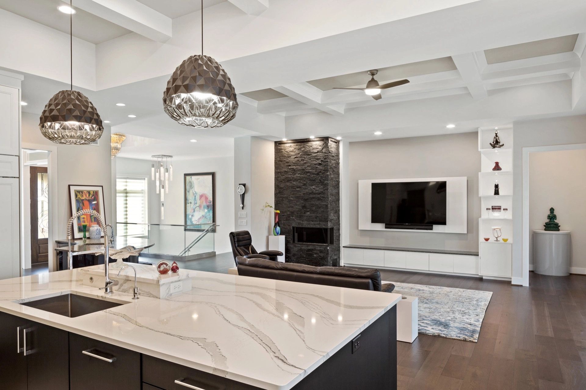 Modern living room with black fireplace, TV, kitchen island, and pendant lights.