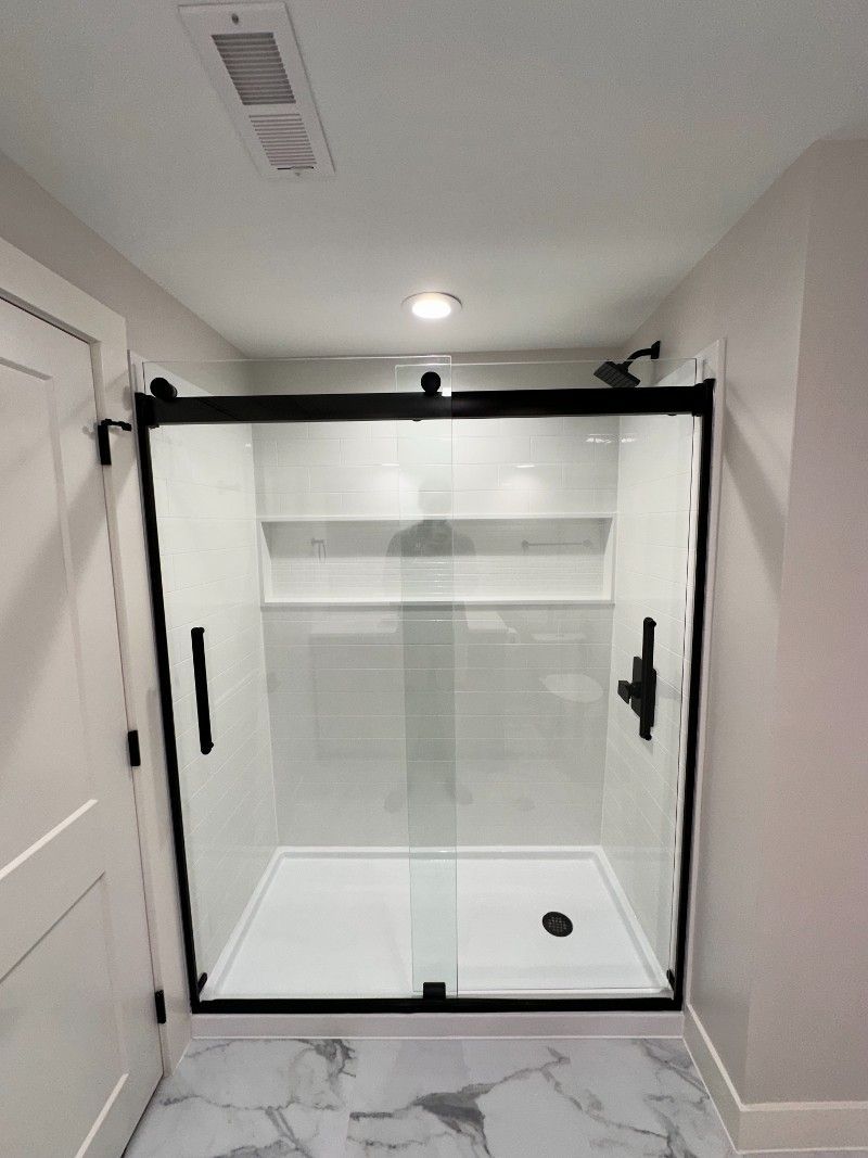 Black-framed glass shower with sliding door, white tile, marble floor.