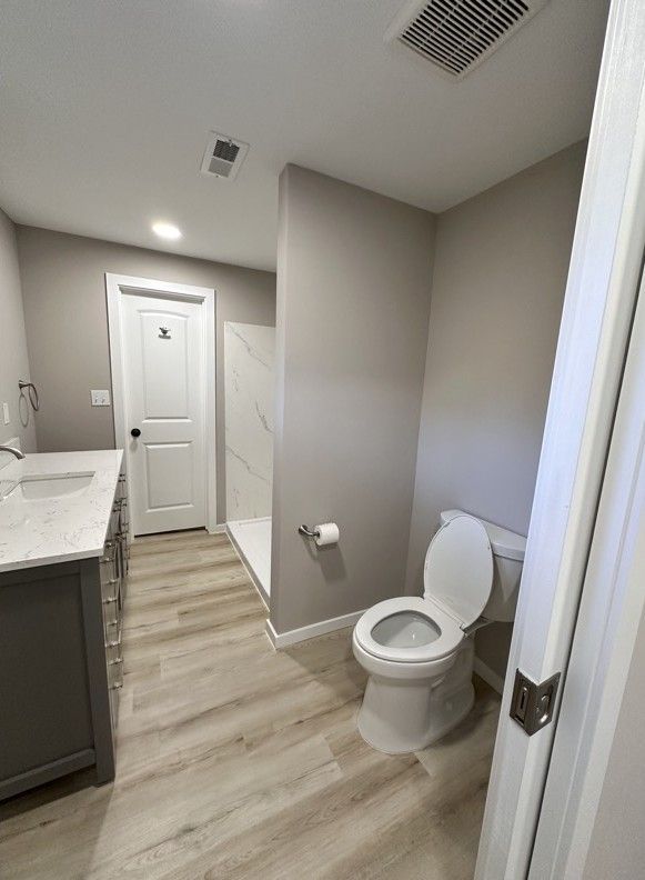 Bathroom with toilet, shower, vanity, and wood-look floor. Gray walls and white fixtures.