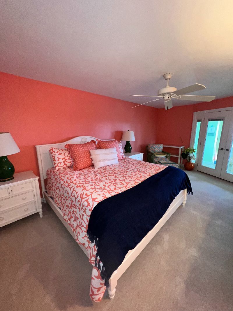 Bedroom with coral walls, white bed, navy blanket, and access to a balcony.