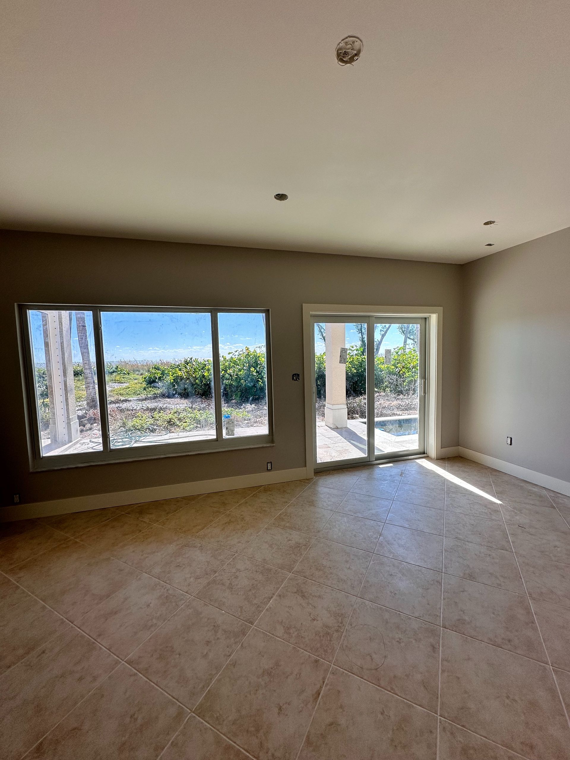 Empty room with tan tile floor, large window, and sliding glass door.  Walls are painted light gray.
