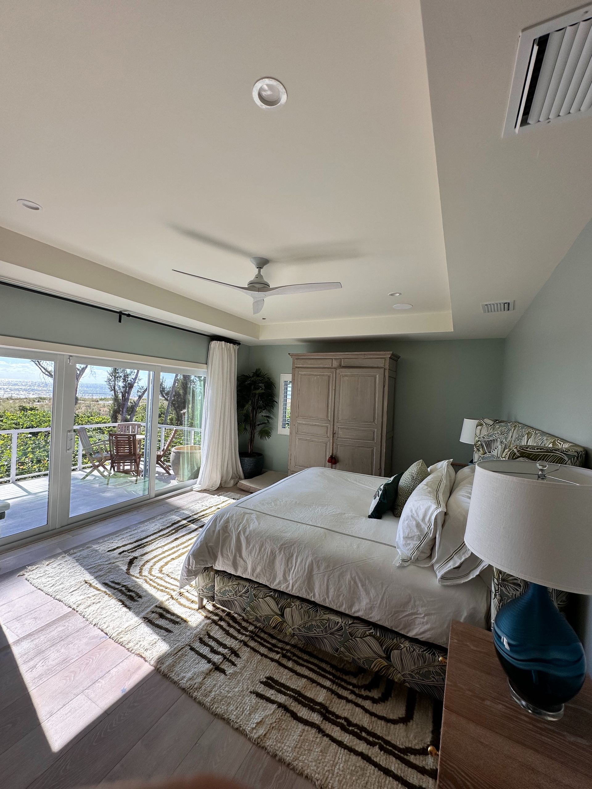 Spacious bedroom with a bed, armoire, and a sliding glass door leading to a balcony with an outdoor view.