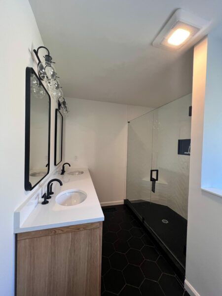 Modern bathroom with a double sink vanity, black hexagon tile floor, and a glass shower.