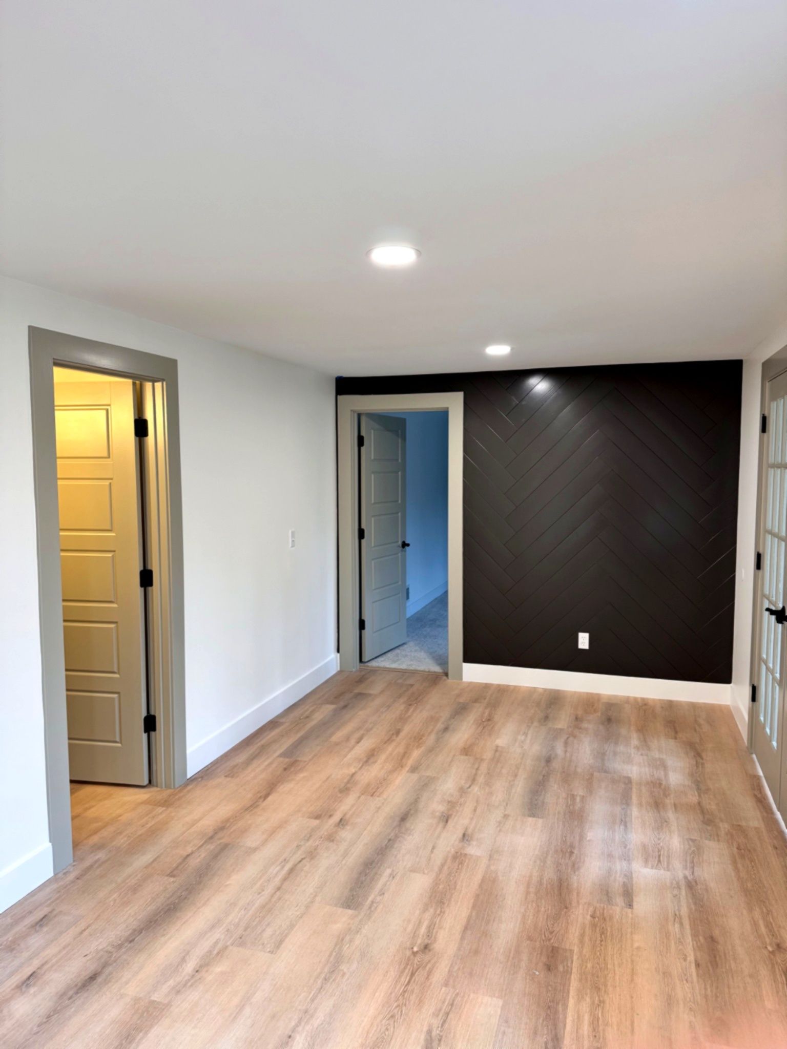 Empty room with wood flooring, black accent wall, and three doorways.