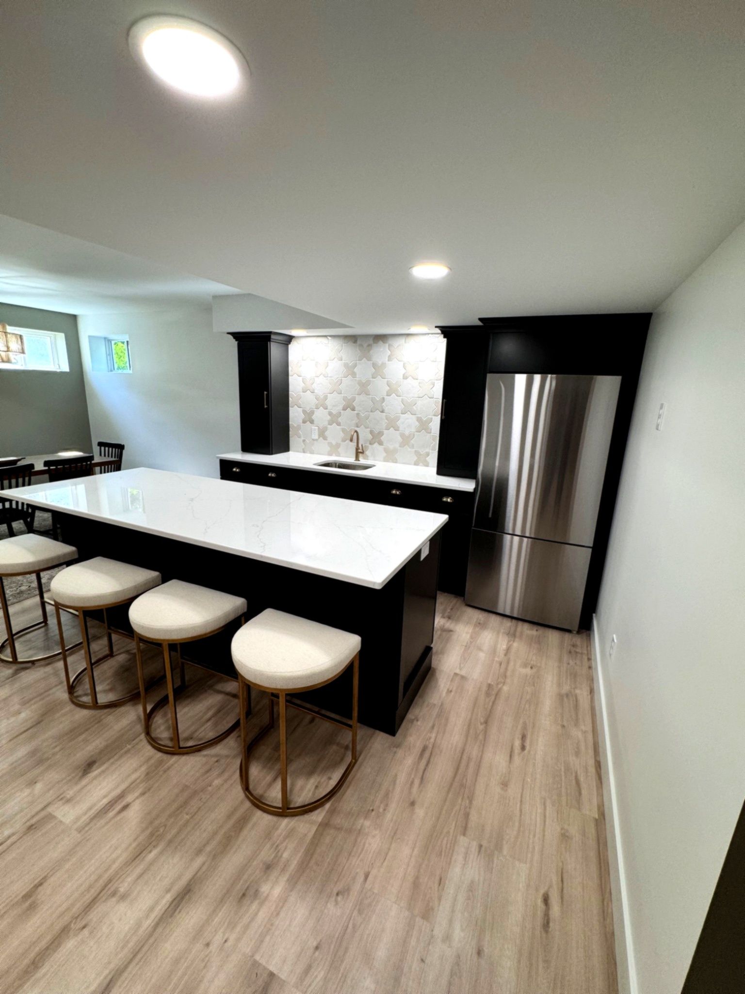 Modern kitchen with a large island, stools, stainless steel fridge, and white countertops.