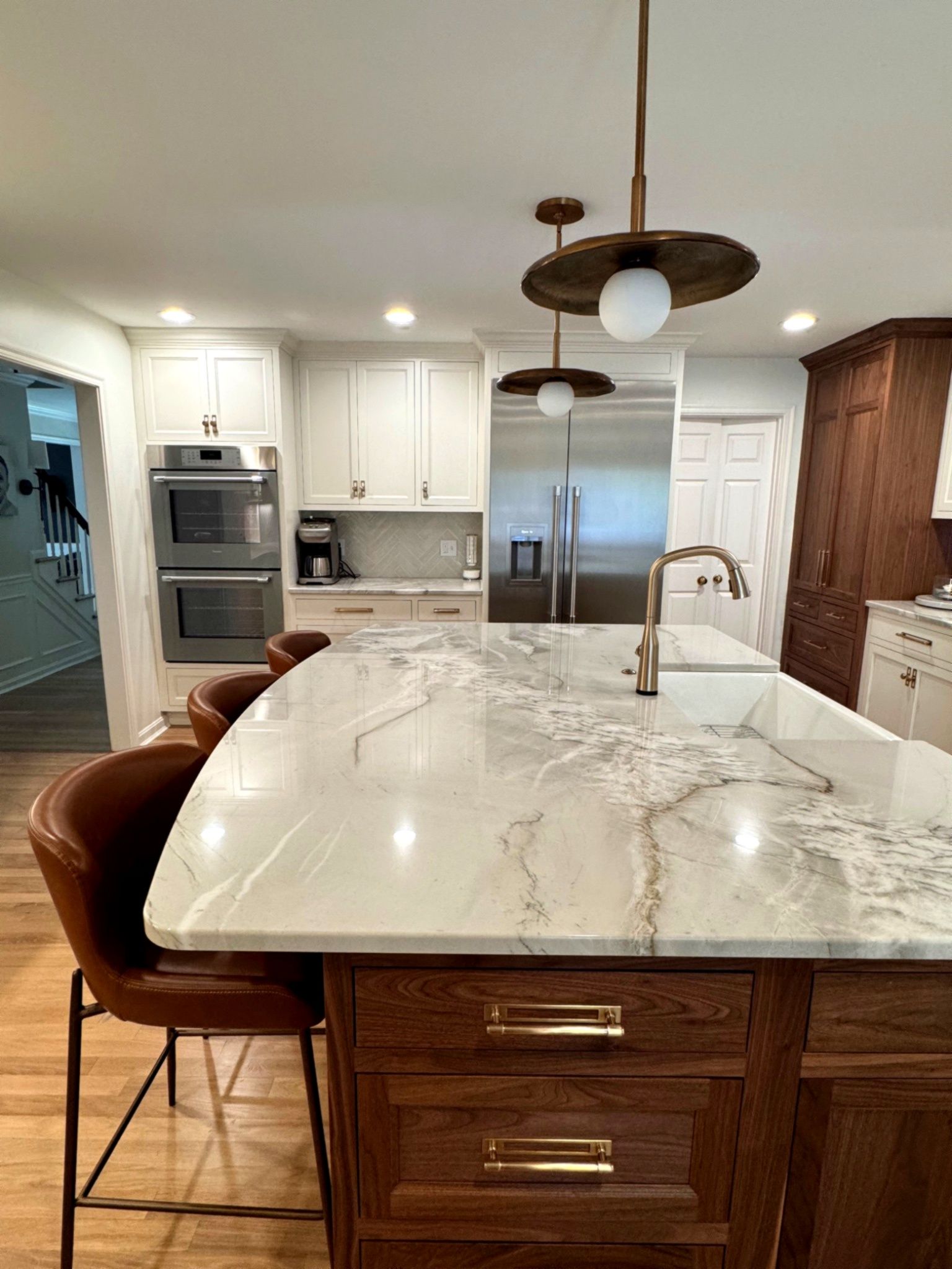 Kitchen with a marble countertop island, brown cabinets, and modern pendant lights.