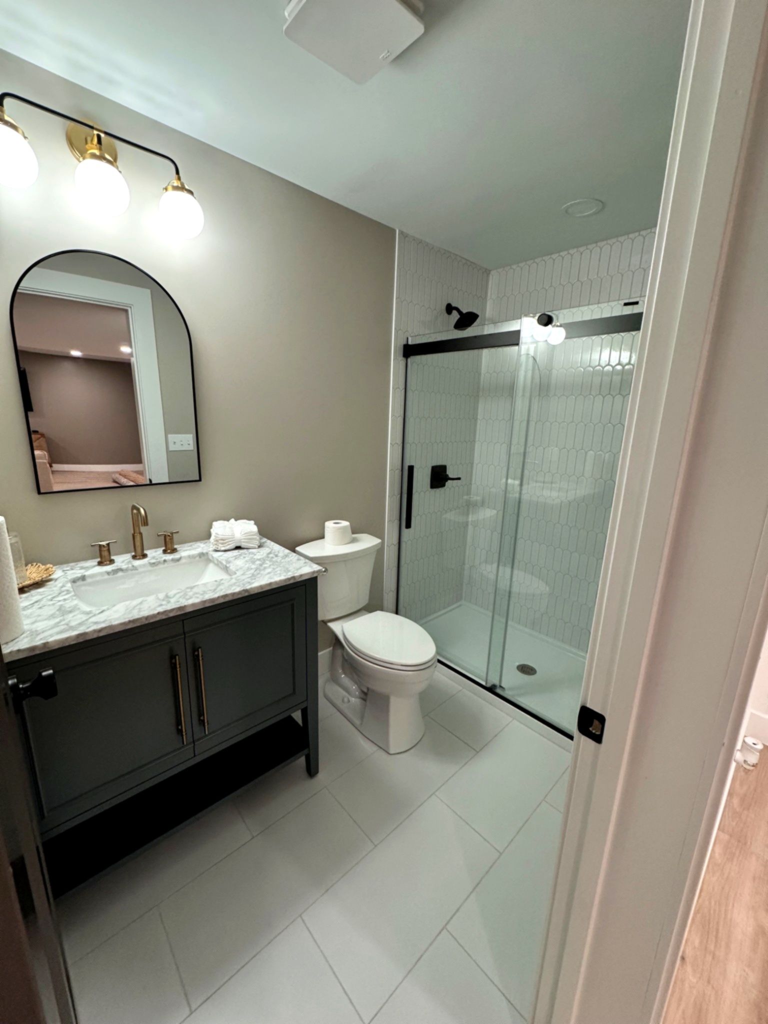 A modern bathroom with a gray vanity, white toilet, and a glass-door shower.