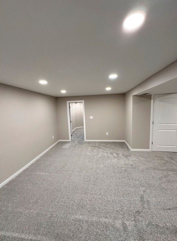 Empty room with gray carpet, beige walls, and white doors/trim; overhead lights illuminate the space.