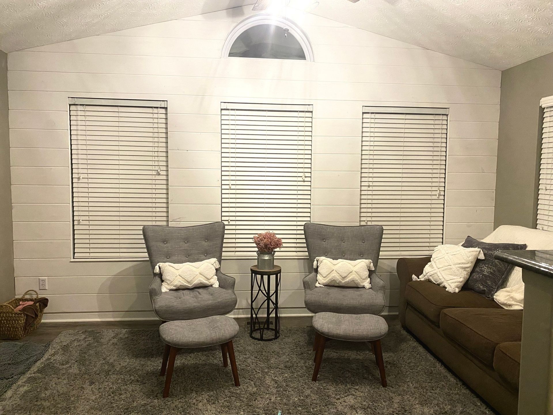 Living room with gray chairs, brown sofa, three windows with blinds, and a white wall.