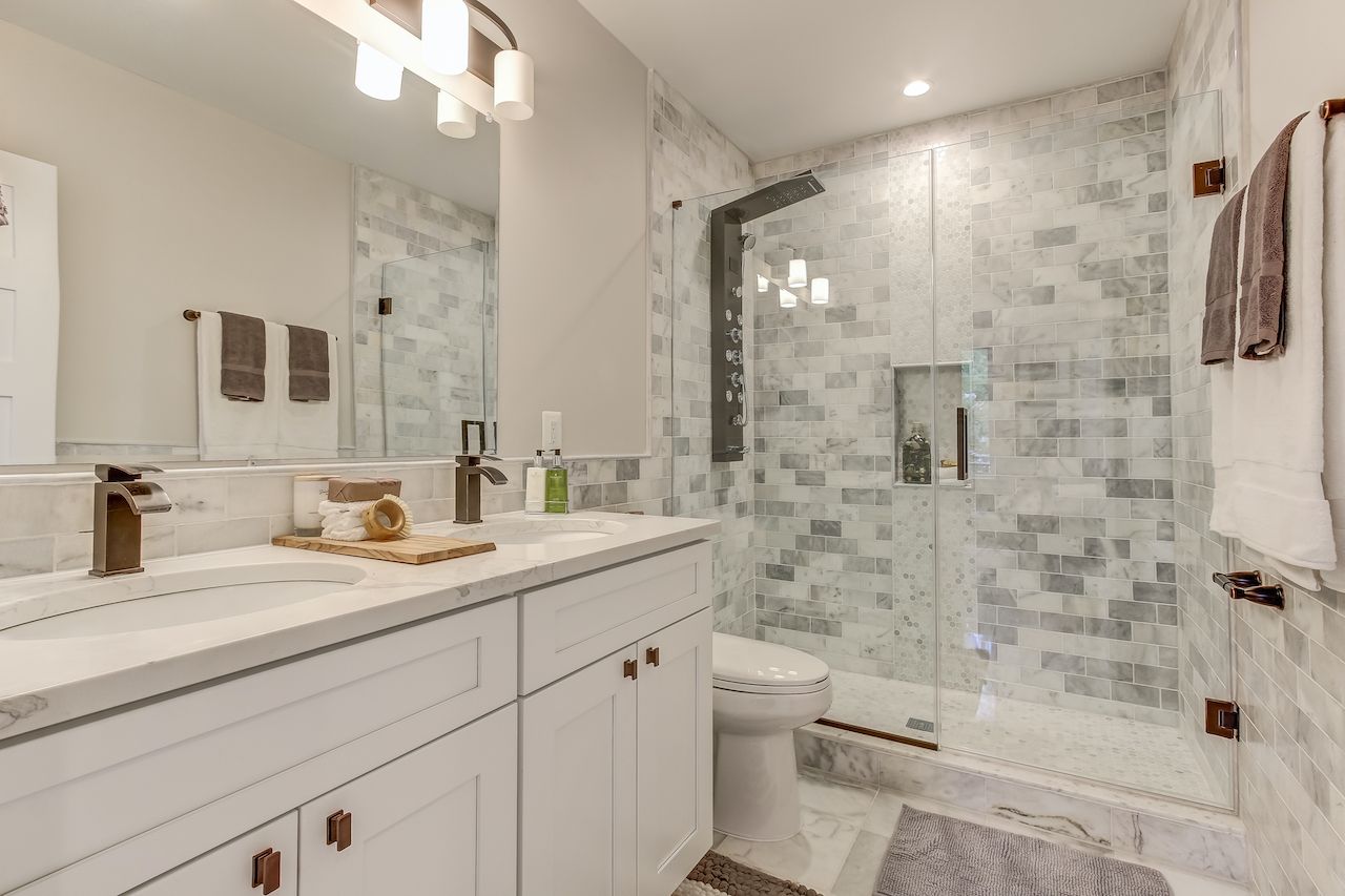 Modern bathroom with white cabinetry, marble shower and walls, and brushed bronze fixtures.