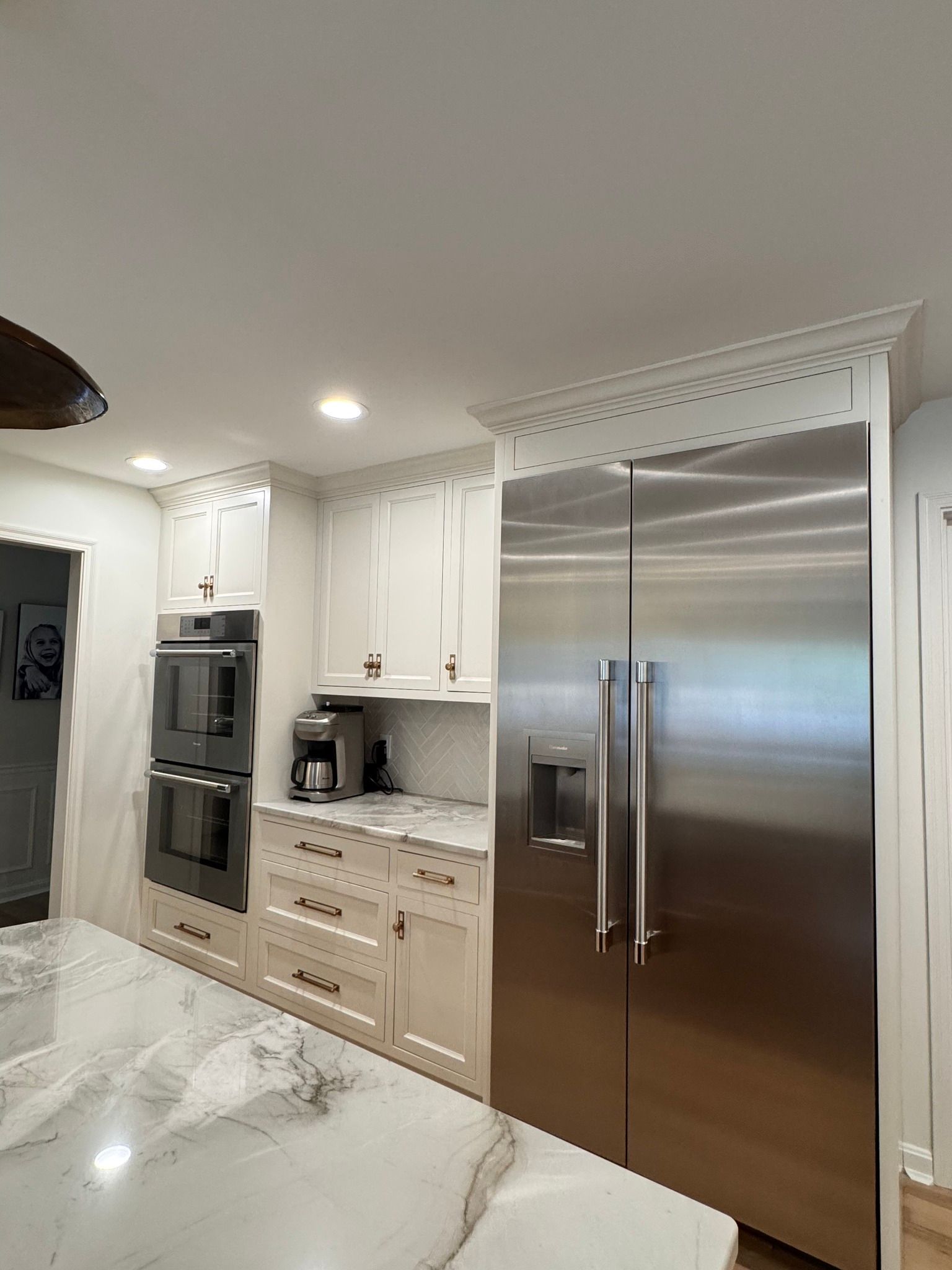 White kitchen with stainless steel refrigerator, oven, cabinets, marble countertop, and recessed lighting.