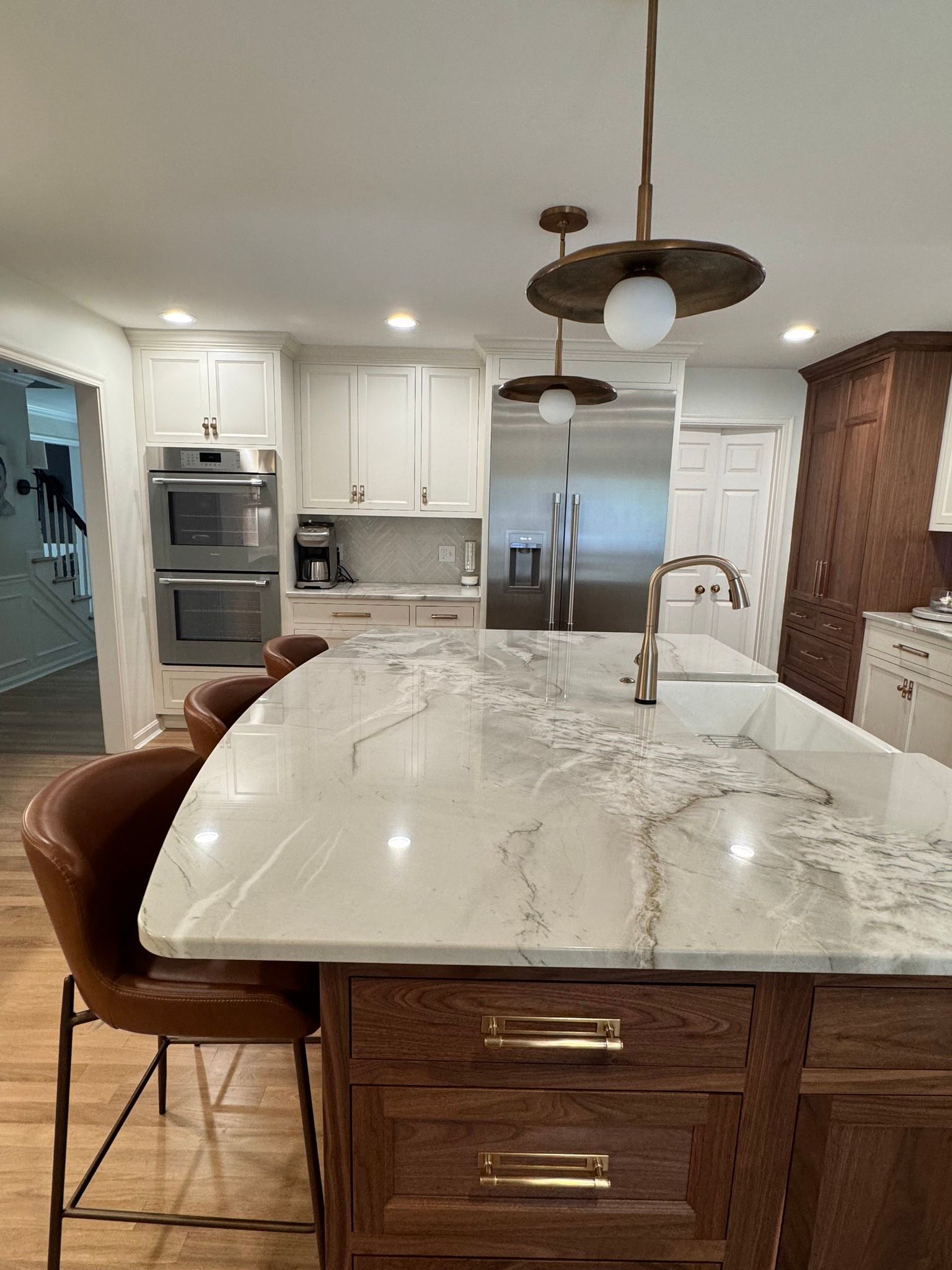 Kitchen with white countertops, wood island, pendant lights, and brown leather bar stools.