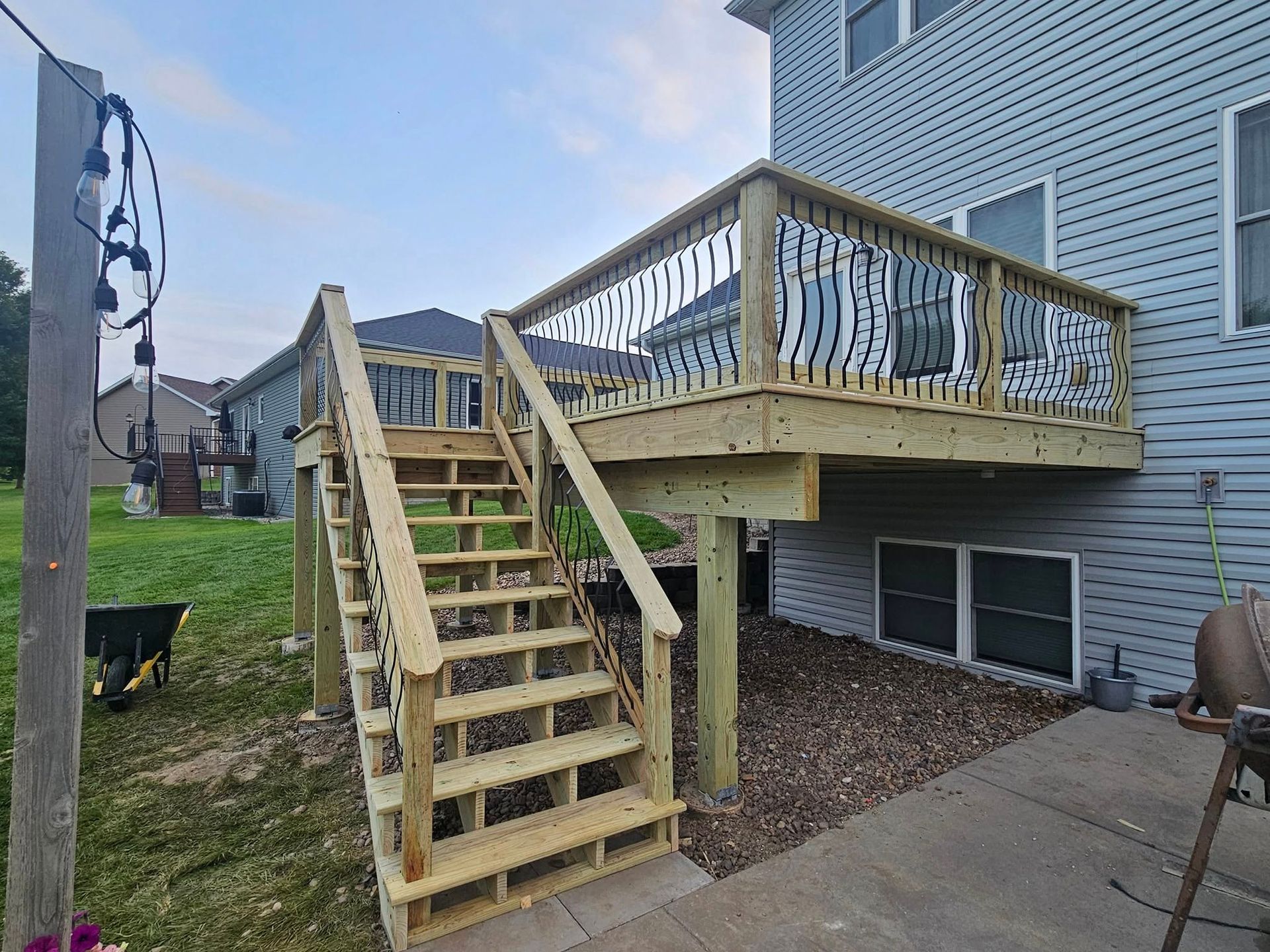 A newly constructed wooden deck and staircase attached to the back of a light blue vinyl-sided house.
