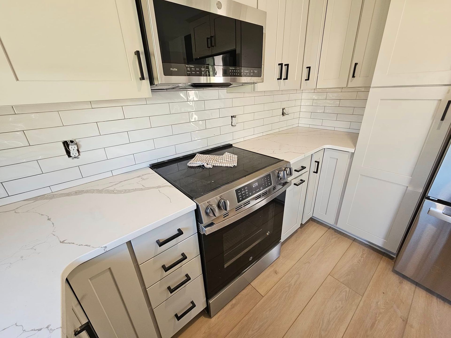 A modern kitchen featuring light cabinets, white marble-patterned countertops, subway tile backsplash, and appliances.