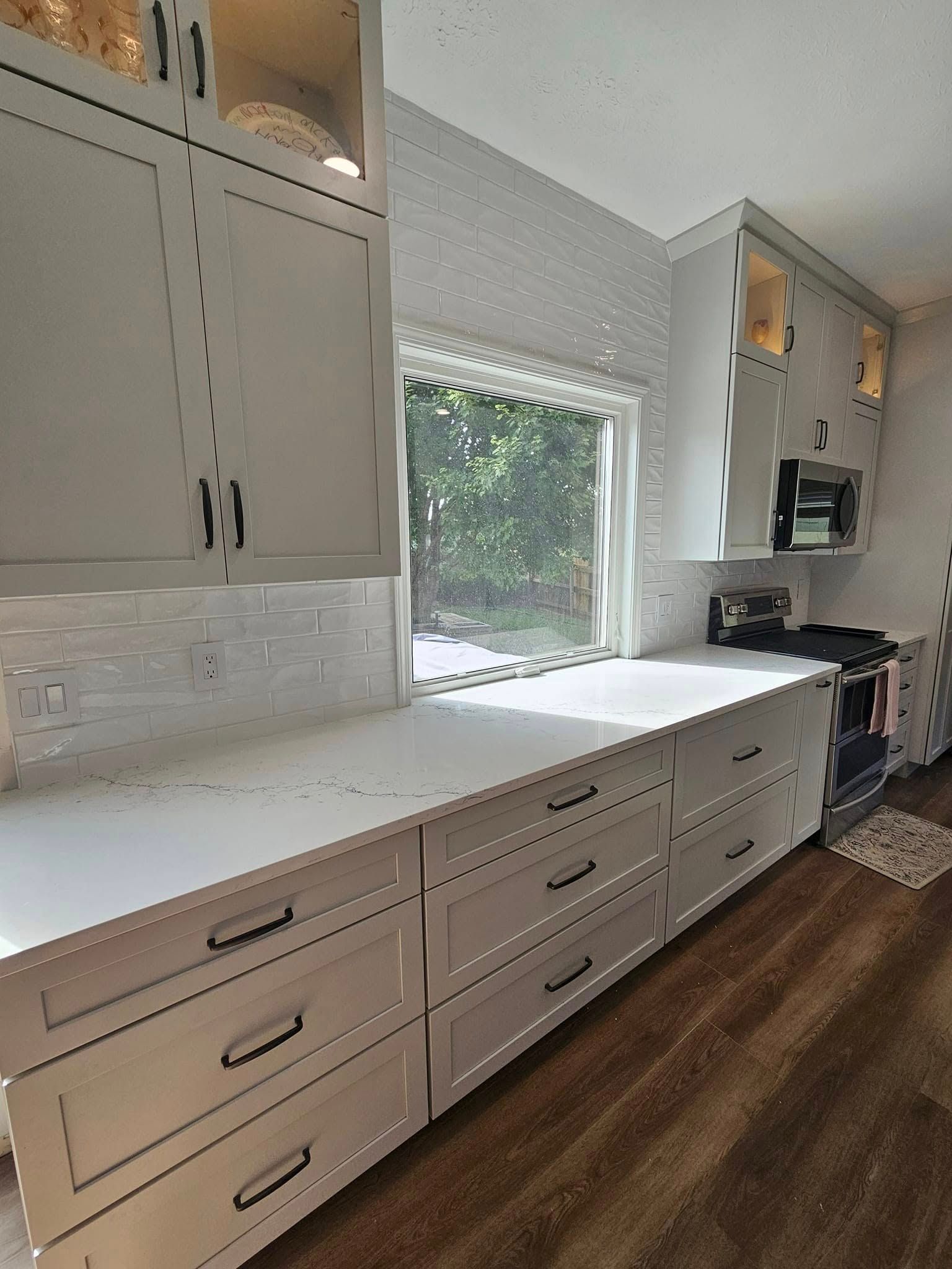 A modern kitchen featuring off-white shaker cabinets, a white quartz countertop, a subway tile backsplash, and wood floors.