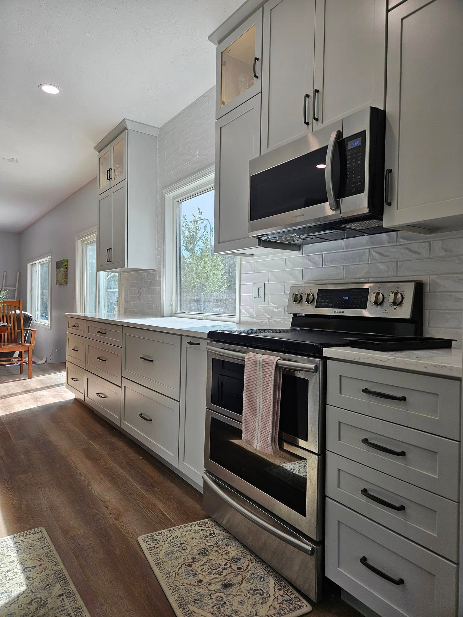 A modern kitchen with grey cabinetry, a stainless steel stove and microwave, white tile backsplash, and wood-look flooring.