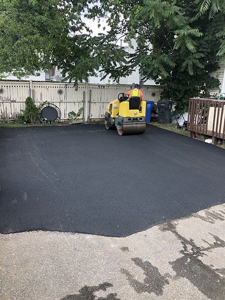 A yellow roller is rolling asphalt in a driveway.