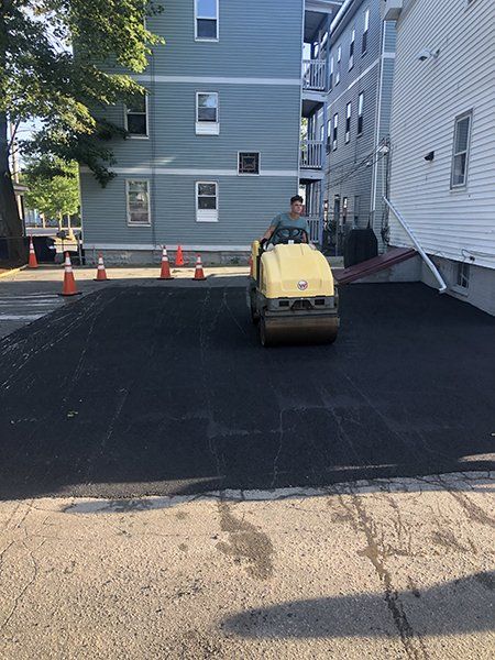 A man is driving a roller on a road in front of a building.