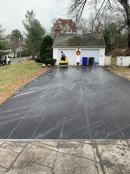 A man is sitting on a roller in a driveway next to a garage.