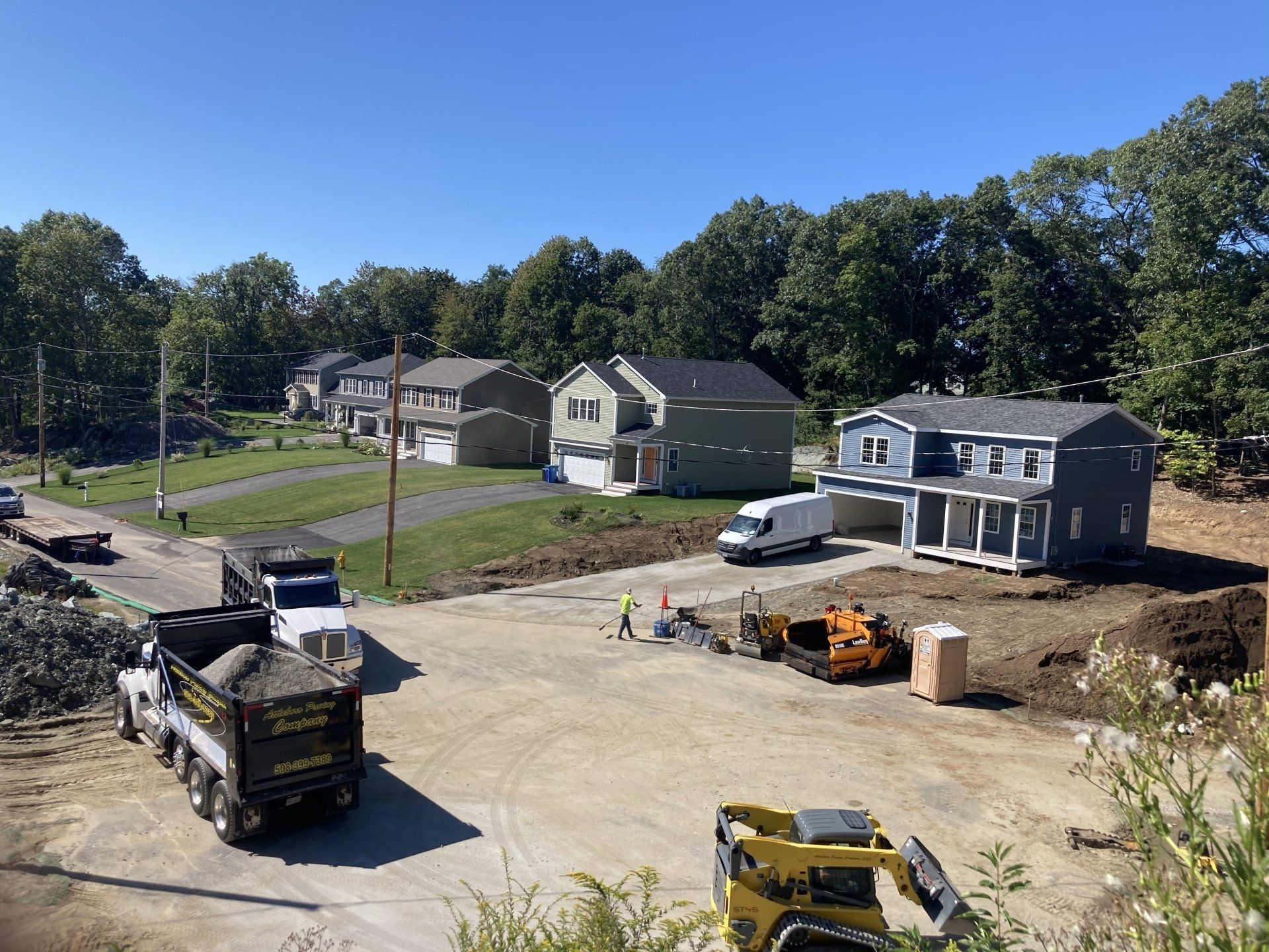 A construction site with a lot of trucks and a house in the background.