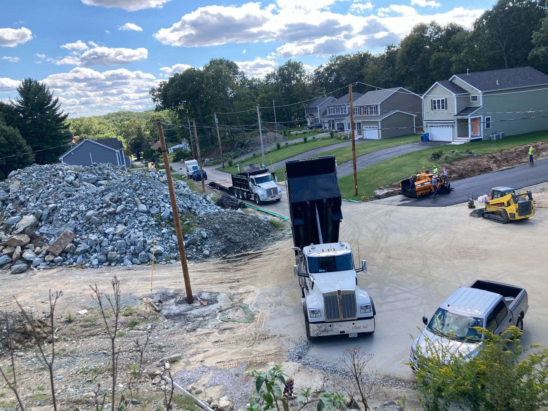 A dump truck is driving down a dirt road next to a pile of rocks.